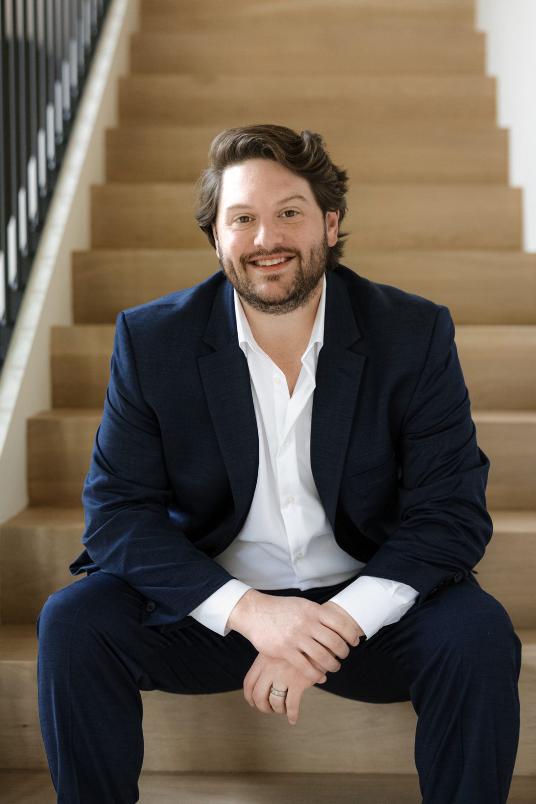 Smiling Nashville real estate agent seated on modern wood stairs—trusted by first-time home buyers and families relocating to Nashville from out of state. Specializes in affordable homes near East Nashville, luxury real estate in Belle Meade, private estate homes in Franklin, and gated communities with new construction in 2025. Your local expert on the cost of living in Nashville vs Atlanta and how to buy your first home with down payment assistance.